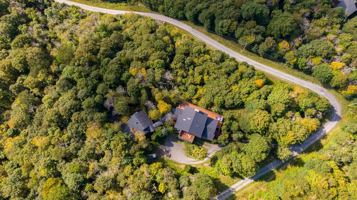 A wide view of the property’s main house surrounded by lush trees and a winding road, suggesting ample outdoor space and a natural environment ideal for exploration. The setting is peaceful and expansive, hinting at open land waiting to be discovered.