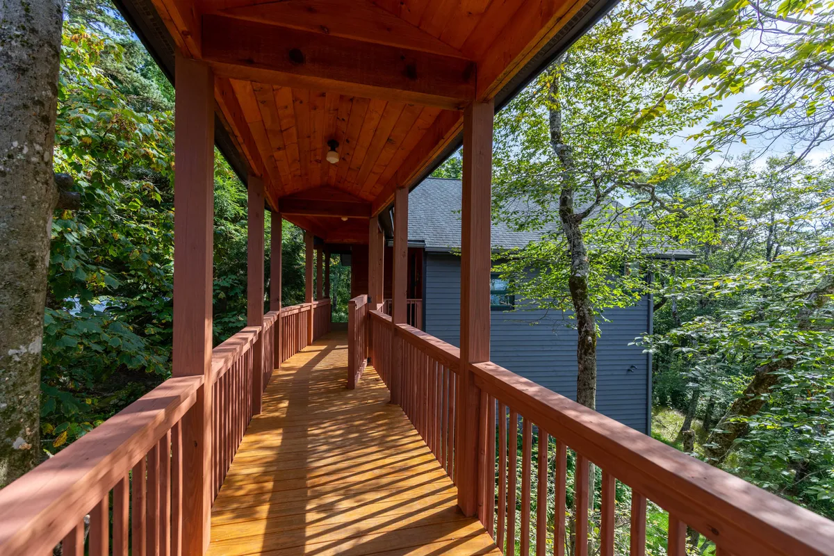 A wooden sky bridge with overhead beams stretches through leafy trees, creating a direct connection between two separate buildings. The tranquil scene is surrounded by greenery, conveying both privacy and unity.