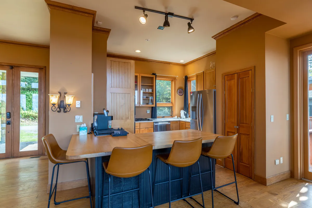 The kitchen is highlighted here, with a spacious island, bar stools for casual conversation, and ample wooden cabinetry. Large windows allow natural light to pour in, making the space bright and inviting—a hub for both cooking and gathering.