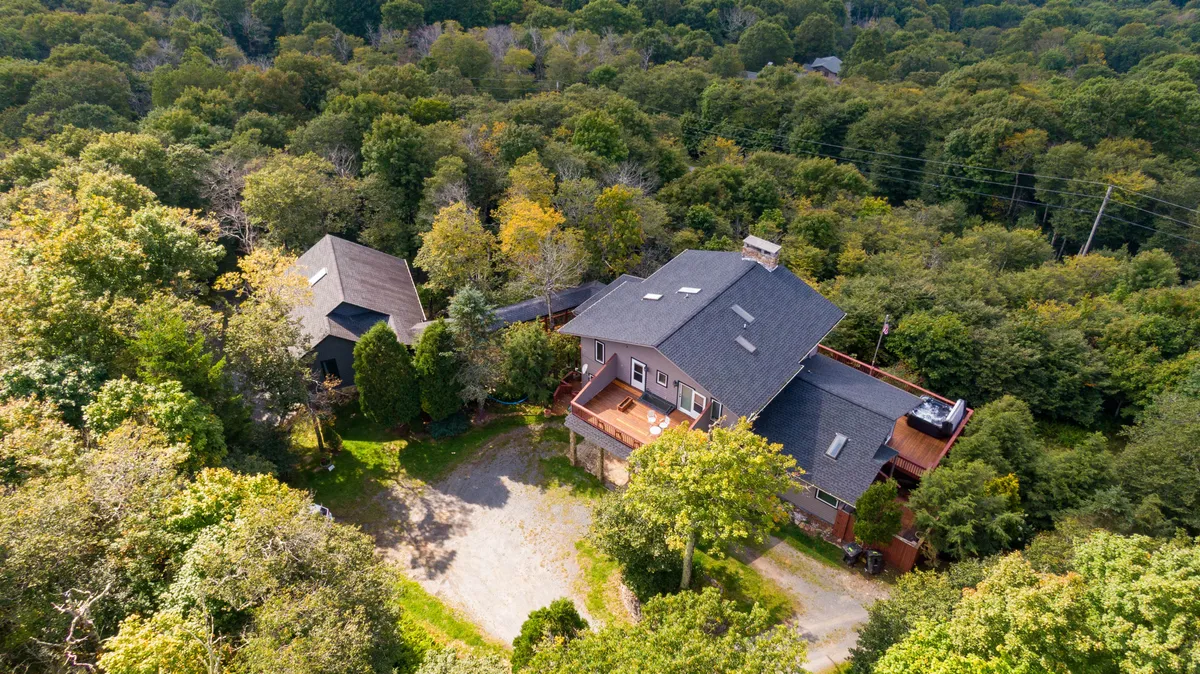 This exterior shot features the main house nestled among tall trees with an inviting deck area. The image captures the peaceful mountain setting and hints at the opportunities for outdoor activities, relaxation, and enjoying the changing seasons.