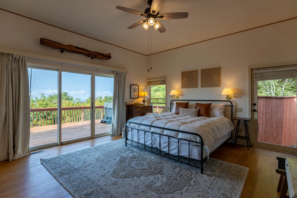 A serene bedroom with a comfortable bed positioned near sliding glass doors, allowing for stunning sunrise views. The room is decorated simply with calming wall art and practical nightstands with lamps, capturing a sense of calm and escape.