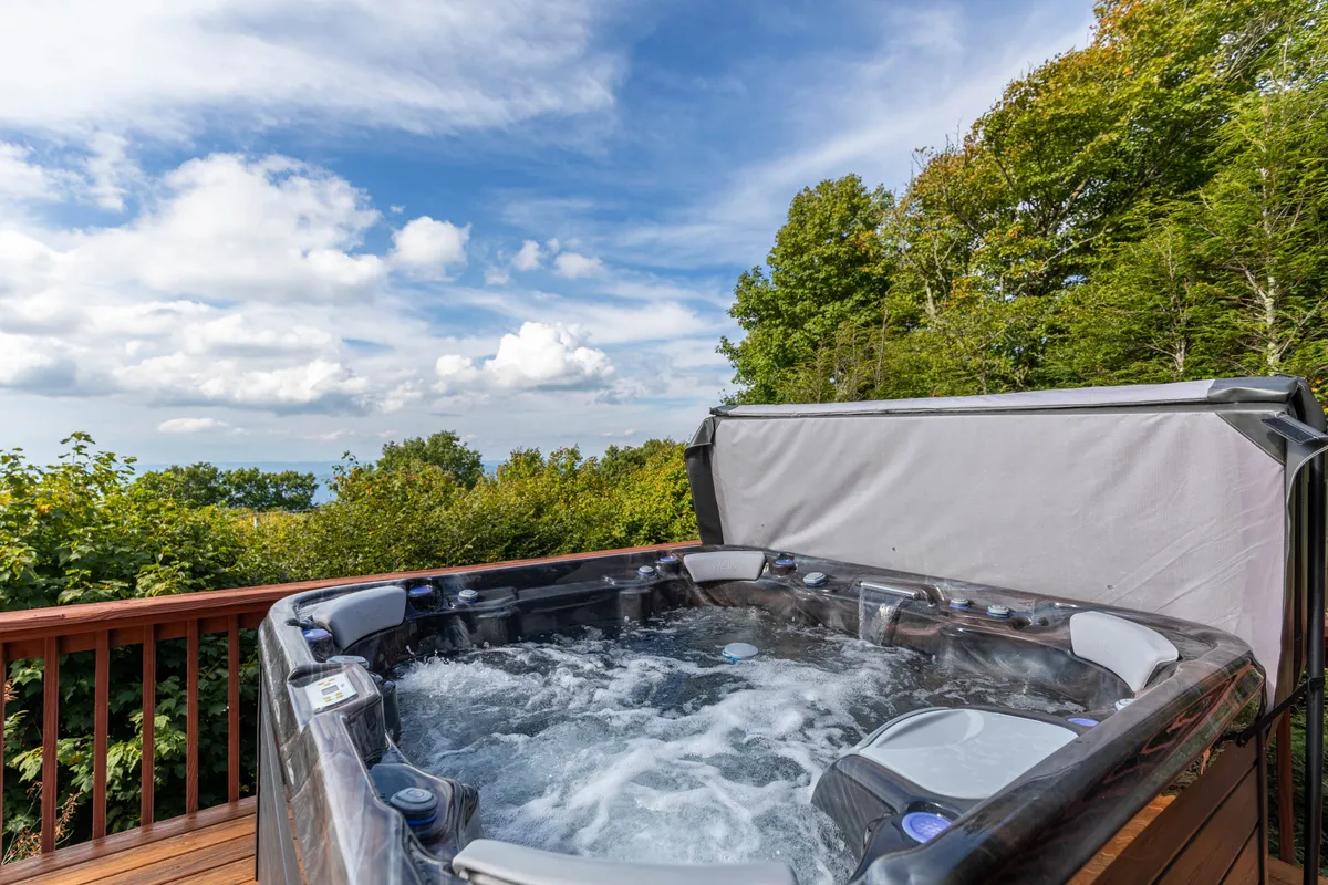 An exterior view highlighting the hot tub, set amid lush greenery with an open sky above. The atmosphere is serene, suggesting relaxation and immersion in nature, ideal for unwinding after adventures like skiing or hiking.