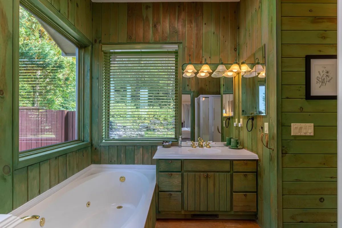 A spa-inspired ensuite bathroom with a freestanding bathtub, a large window bathing the space in natural light, and a well-appointed vanity. The view outside enhances the atmosphere of relaxation and luxury.