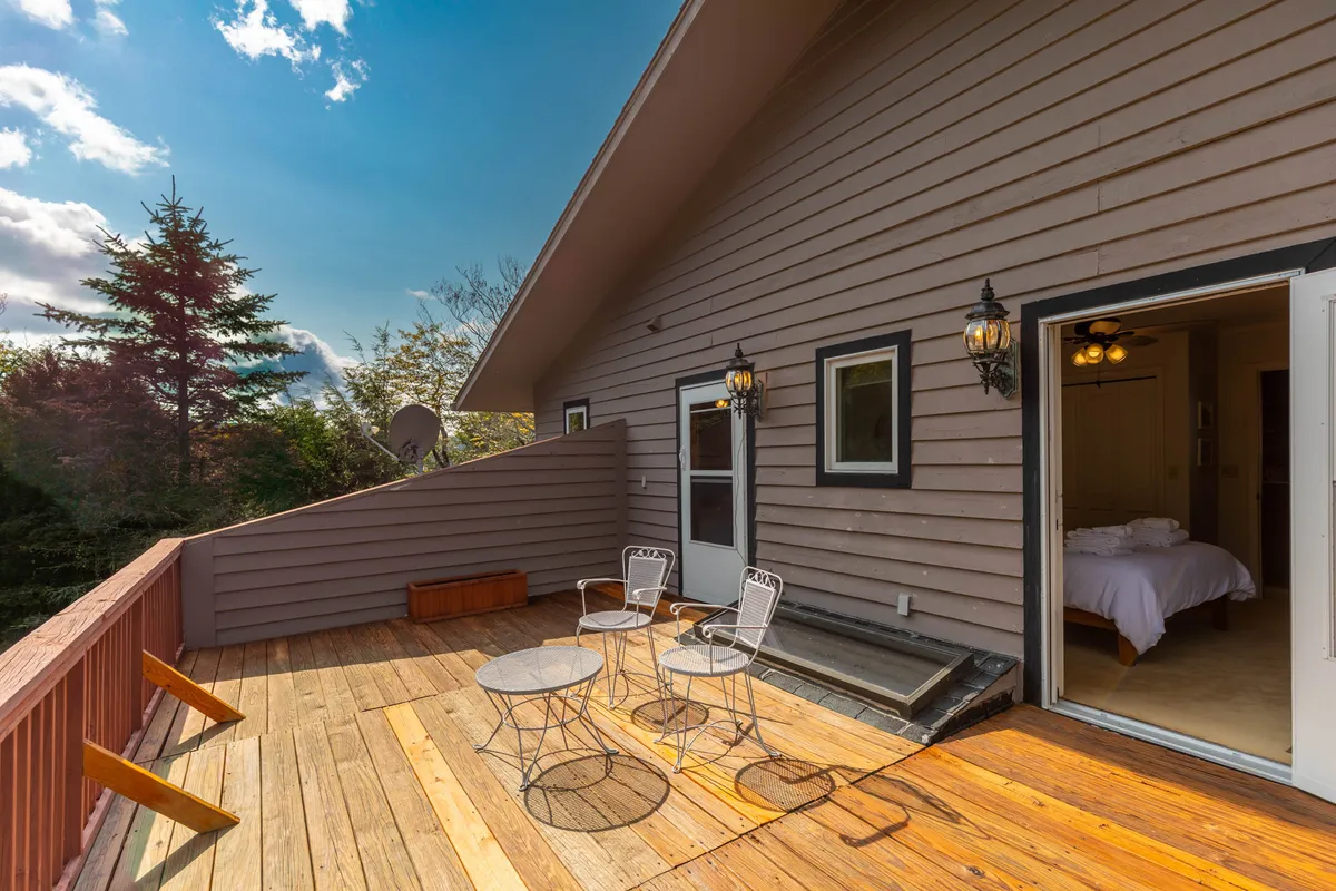 An inviting outdoor deck features comfortable chairs and a table, with a doorway leading into the home. The setting is tranquil, perfect for sipping coffee while watching the sunrise or relaxing after a day of adventure.
