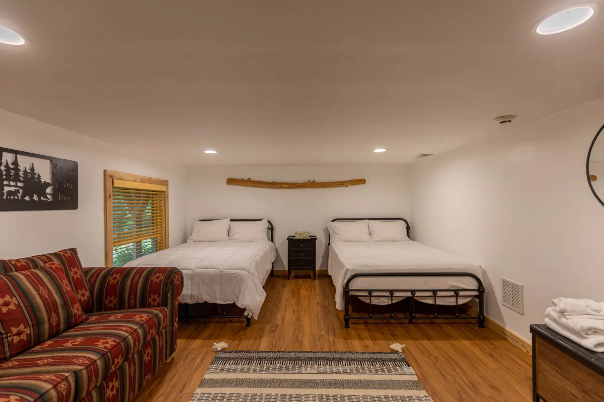 A flexible bedroom setup featuring two double beds and a striped sofa, with exposed wooden beams adding a touch of rustic charm. The shared, casual space feels adaptable for younger travelers or extra guests and encourages both relaxation and socializing.