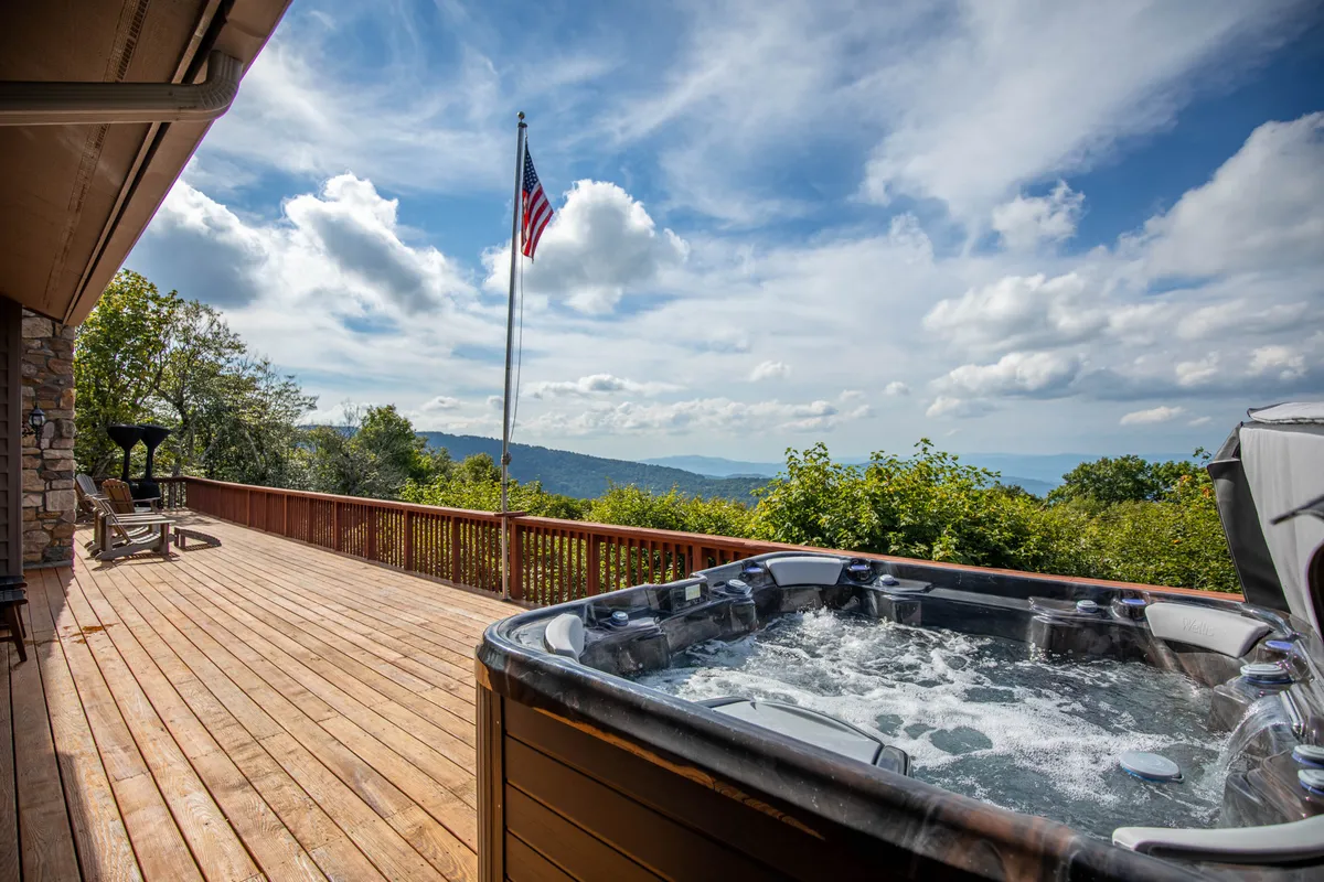 A tranquil hot tub on a spacious deck overlooks distant mountains and a wide-open sky. The American flag and wooden elements emphasize a sense of place and adventure. The setting is ideal for relaxing after an active day, with the expanse of the mountains serving as a constant reminder of the region’s outdoor possibilities.